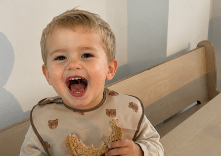 Lachende peuter met een boterham aan tafel